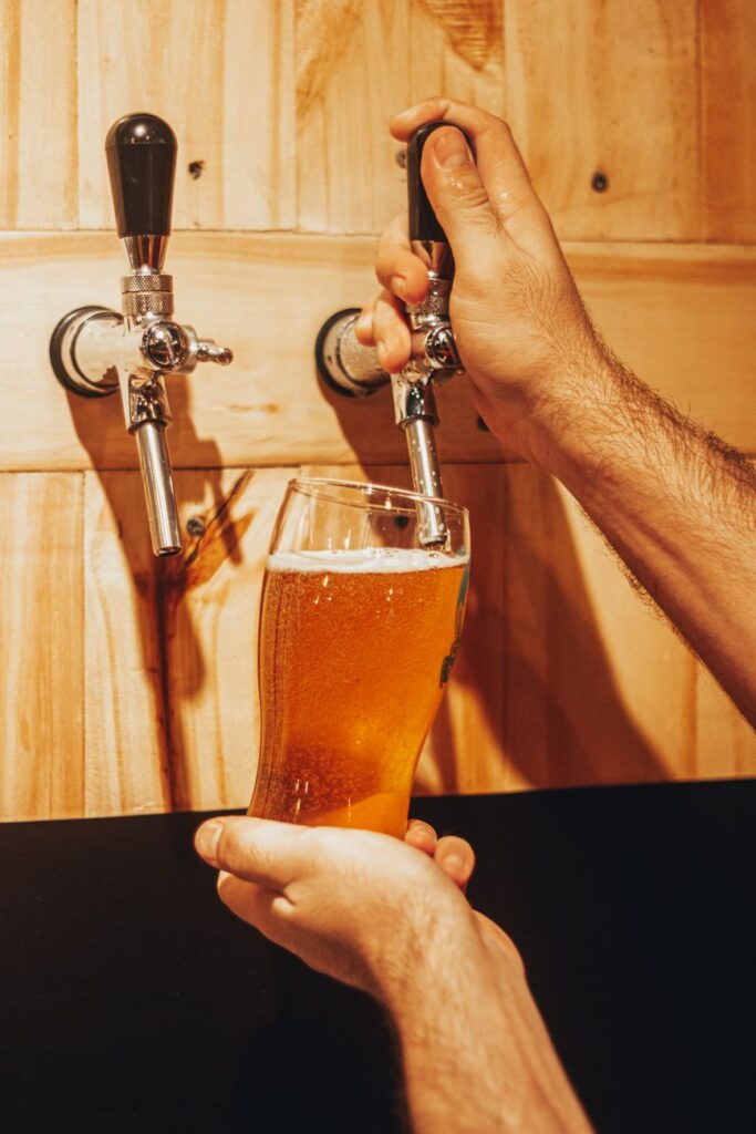 A person pouring refreshing craft beer into a glass from a tap against a wooden wall.