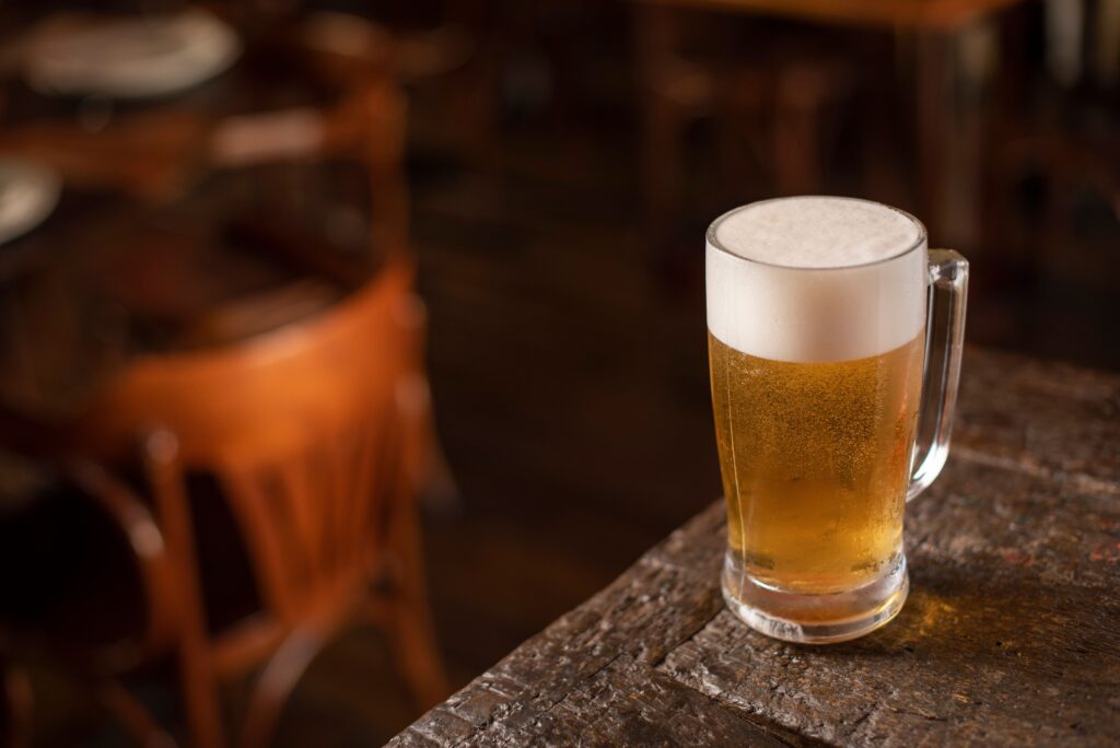 A cerveja que você gosta diz algo sobre você? Talvez menos do que você imagina. Close-up of a frothy beer mug on a wooden table in a cozy pub setting.